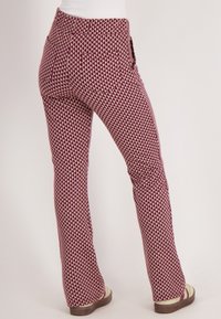 Uitlopende broeken met een maroon en crèmekleurig driehoekig patroon, gemaakt van een textuurstof en met zijzakken. Gedragen met lichte sandalen.