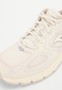Bottines de sport beiges avec des panneaux en maille et des accents en daim. Bout rond, semelle épaisse et lacets texturés. Détail réfléchissant notable sur le côté.