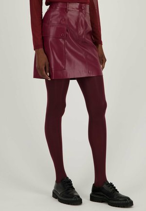 Bordeaux faux leren rok met zijzakken, gecombineerd met bijpassende panty’s en zwarte veterschoenen met een dikke zool.