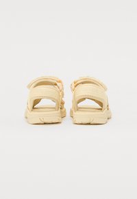 Sandales beige clair avec des brides réglables, un matériau supérieur texturé, des semelles larges et une semelle intérieure rembourrée. Possède des détails de couture bien définis.