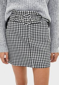 Černobílá sukně s kostkovaným vzorem a vysokým pasem, doplněná kulatými knoflíky. Materiál vypadá jako tkaný a má hladkou strukturu.
