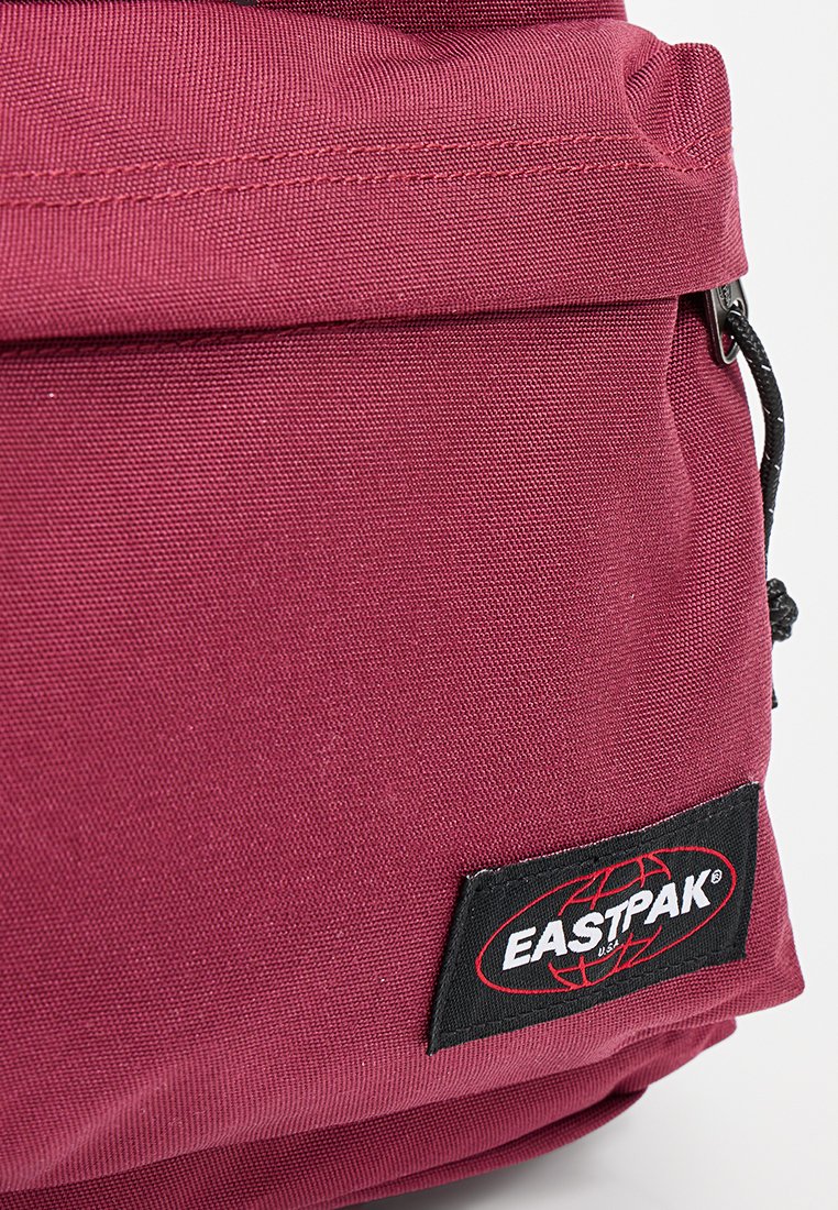 Roter Stoffrucksack mit strukturierter Oberfläche, ausgestattet mit einem auffälligen Eastpak-Logo-Patch. Beinhaltet verstellbare Träger und eine Reißverschlusstasche.