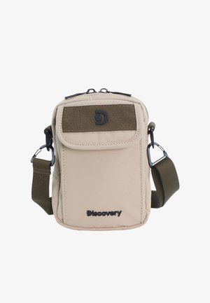 Beige kompakte Umhängetasche mit vorderer Klappentasche, verstellbarem olivgrünem Riemen, schwarzem Discovery-Logo und Reißverschluss oben.