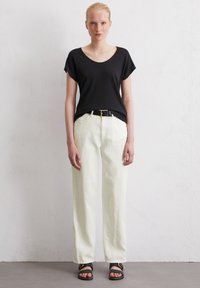 T-shirt noir à encolure dégagée, coupe ample, associé à un pantalon large crème et à des sandales plates noires avec des accents dorés. Texture lisse sur l'ensemble.