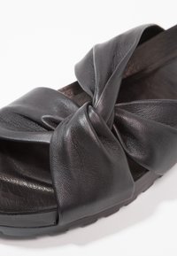 Sandale à enfiler en cuir noir avec un design de nœud torsadé sur le dessus et une semelle rembourrée.
