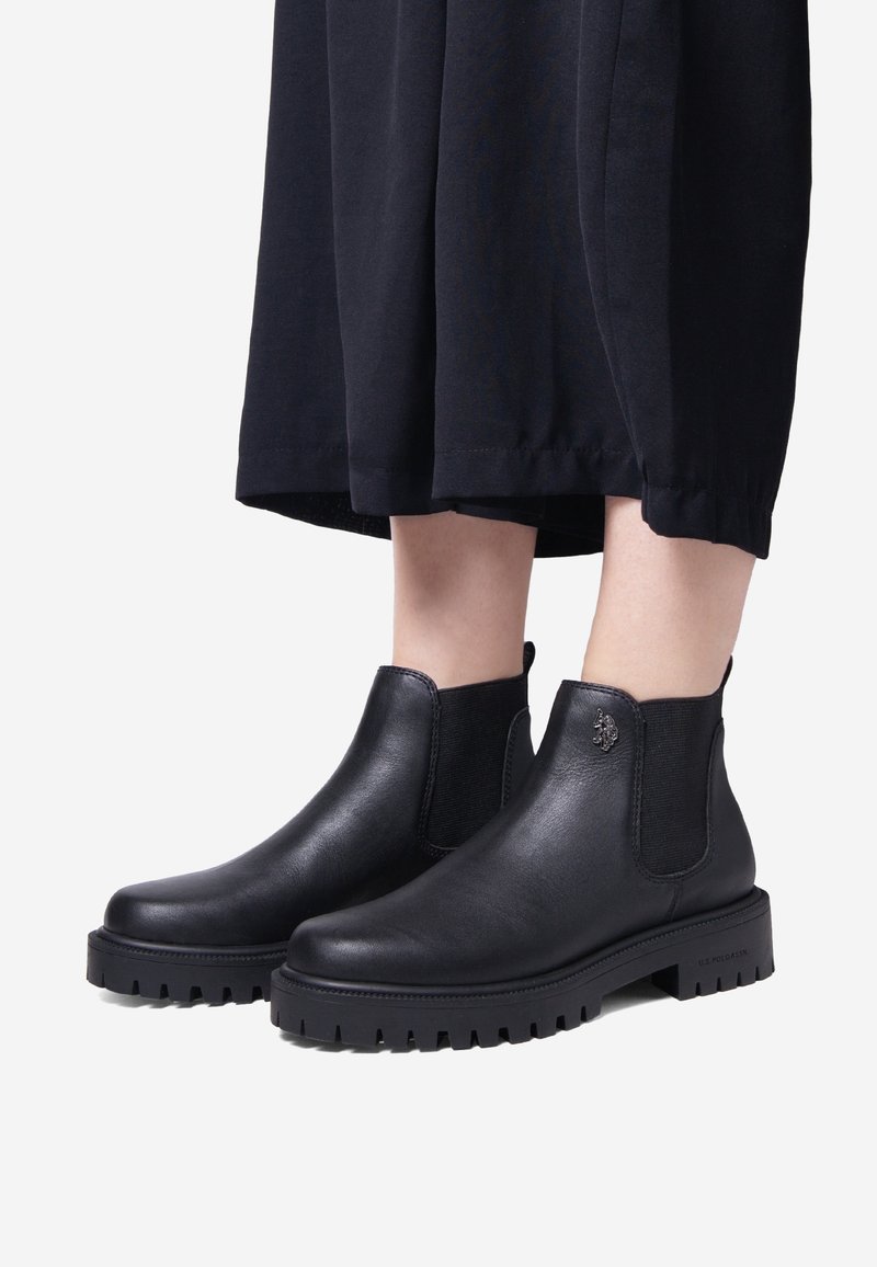 Botas Chelsea de cuero negro con paneles laterales elásticos, punta redondeada y suela resistente. Detalle de logo notable en el costado.