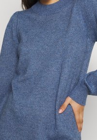 Maglione blu lavorato a maglia con scollo rotondo, maniche lunghe e polsini a coste. Texture morbida con leggere variazioni di colore.
