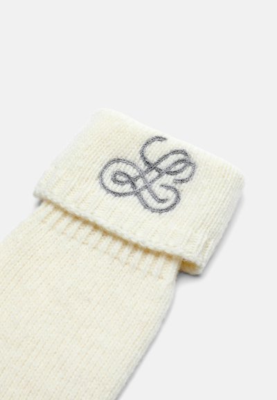 Krämfärgad stickad strumpa med vikskaft. Har en grå broderad logotyp påskaftet. Ribbad struktur över hela strumpan.