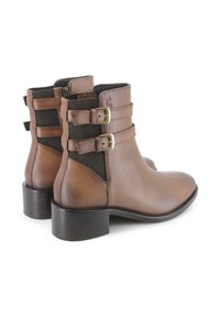 Botas de tobillo de cuero marrón con correas de doble hebilla, paneles laterales elásticos y un moderado tacón apilado, que ofrecen una silueta elegante y ajustada.