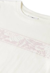 Biała koszulka z jasnoróżowym kwiatowym wzorem na wysokości klatki piersiowej, z okrągłym dekoltem i miękką, teksturowaną tkaniną.