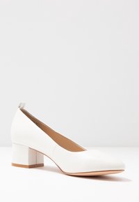 Vita läder pumps med blockklack och spetsig tå, slät yta och minimalistisk design. Har en låg, fyrkantig klack för stabilitet.