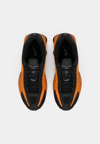 Sapatilhas Nike Shox em preto e laranja, com um cabedal texturizado, biqueira redonda, sistema de laço e detalhes de marca característicos na língua.