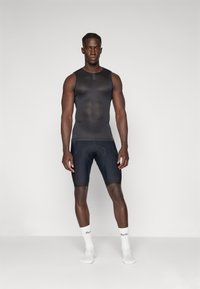 Schwarzes Sportoberteil mit rundem Ausschnitt, kombiniert mit dunklen Radshorts mit gepolsterter Einlage. Weiße Socken mit Logo-Detail.