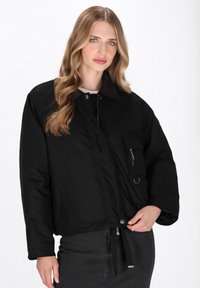 Giacca nera cropped con tasca con zip, bottone a pressione e orlo regolabile; presenta un colletto testurizzato e una finitura in tessuto liscia.