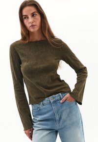 Camiseta de manga larga en verde oliva, con un acabado texturizado y un cuello redondo, combinada con unos vaqueros azul claro de corte relajado.