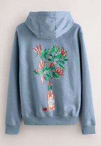 Lyseblå hættetrøje med en grafik af en Tabasco-flaske med røde chilipebre og grønne blade, der vokser fra toppen.