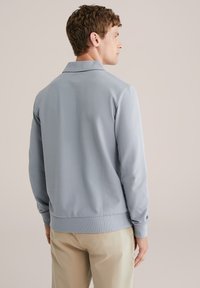 Light blue long-sleeve polo shirt with a collar. Features ribbed cuffs and hem, made from a smooth fabric. Plain design, no patterns.