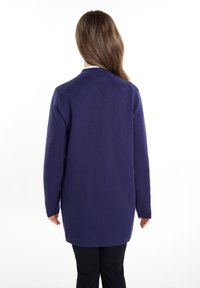Cardigan a maniche lunghe, di un solido viola scuro, realizzato in tessuto morbido, con un taglio dritto e senza chiusure o motivi visibili.