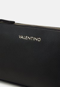 Fekete textúrájú bőr cluth, arany cipzárral és domború "VALENTINO" logóval. Simább felület jellemzi, kompakt, téglalap alakú. 