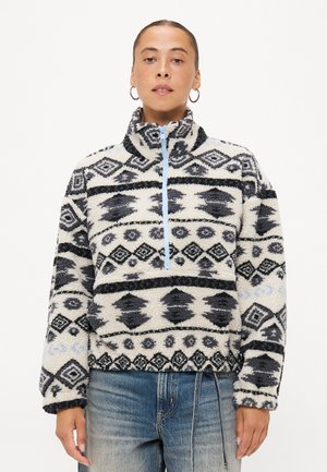 Fleece-pullover med halvglidelås, med et geometrisk mønster i svart og hvitt, lyseblå glidelås, og en myk, teksturert finish.