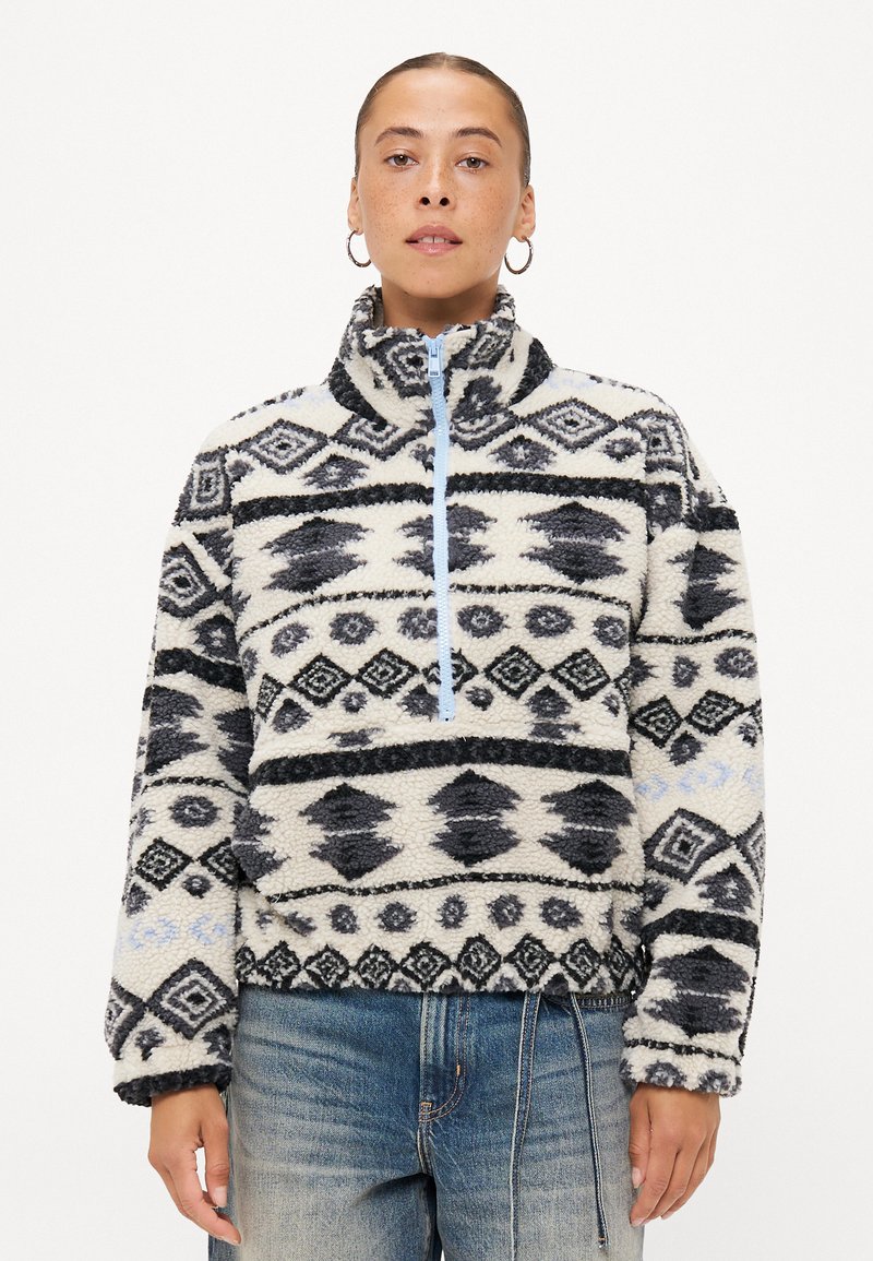 Fleece mikina s polovičním zipem, která má geometrický vzor v černé a bílé barvě, světle modrý zip a měkký, strukturovaný povrch.