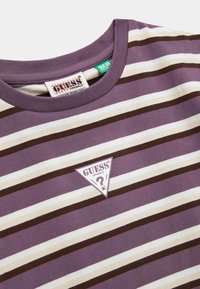 Fioletowa, biała i brązowa koszulka z okrągłym dekoltem w paski z naszywką logo Guess Originals w kształcie trójkąta oraz etykietą z logo w kołnierzyku.