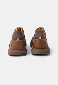 Zapatos de ante marrón con tacón de cuero y acentos naranjas. Presentan un diseño redondeado, una superficie texturizada y detalles de costura en contraste.