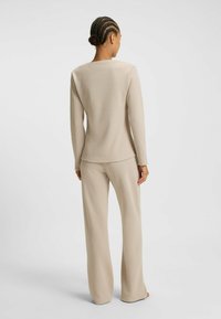 Beige långärmad topp och matchande byxor i en texturerad tyg, med rund halsringning och avslappnad passform, visad bakifrån.
