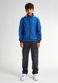 Jachetă albastră cu fermoar, cu textur�ă modelată, manșete și tiv negre. Asortată cu pantaloni cargo negri și adidași albi.