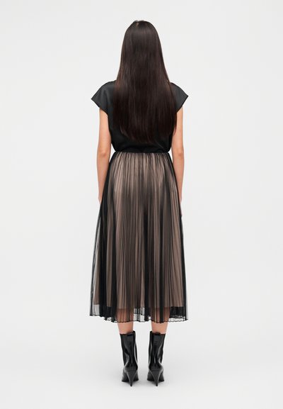 Μαύρο μπλουζάκι με κοντά μανίκια, πλισέ μίντι φούστα σε αποχρώσεις μαύρου και ταουπέ, συνδυασμένη με μαύρα μυτερά μποτάκια αστραγάλου.