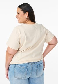 Short-sleeve, beige cotton t-shirt with a round neckline. Paired with medium-wash blue jeans featuring back pockets. Smooth texture.