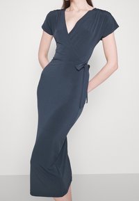 Marineblauwe wikkeljurk van zachte stof, voorzien van korte mouwen, een diepe V-hals, een ceintuur in de taille en een aansluitend silhouet tot op de knie.