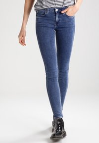 Tunna blå denimjeans med en slät yta, hög midja, fem fickor och kontrasterande sömmar, i kombination med svarta ankelstövlar.