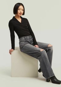 Camisetta nera a maniche lunghe con colletto abbinata a jeans grigi a gamba larga con ginocchia strappate e stivali neri con tacco spesso.