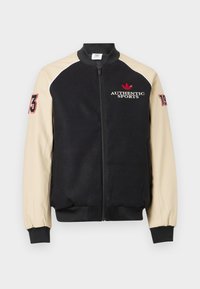 Μαύρο και μπεζ μπουφάν varsity με φερμουάρ μπροστά, κείμενο «AUTHENTIC SPORTS» και κόκκινο λογότυπο στο στήθος, αριθμοί «73» και «19» στα μανίκια.