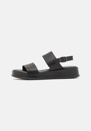 Black leather sandal with two wide straps, a buckle ankle strap, and a thick flat sole, shown in side view on white background.