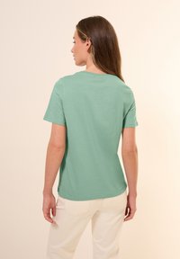 Lys grøn bomulds t-shirt med korte ærmer og rund halsudskæring. Har en afslappet pasform og glat tekstur, vist fra bagsiden.
