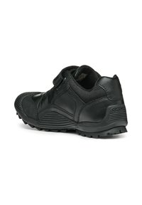 Zapatilla deportiva negra con una tira de velcro, que cuenta con un upper de cuero liso y malla, suela de goma texturada y talón reforzado.