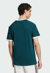 T-shirt à manches courtes vert foncé avec col et bords de manches en côte blanche, présentant un design simple et une coupe décontractée. Texture lisse.