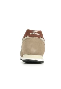 Zapatilla de ante beige con un cuello acolchado marrón y el logotipo "new balance" en blanco. Presenta una suela de goma negra y una entresuela de color crema claro. Diseño clásico.