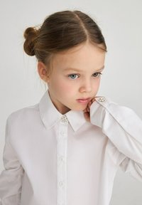 Camicia bianca con colletto e bottoni decorativi in cristallo ai polsini. Tessuto liscio, design classico, maniche lunghe.