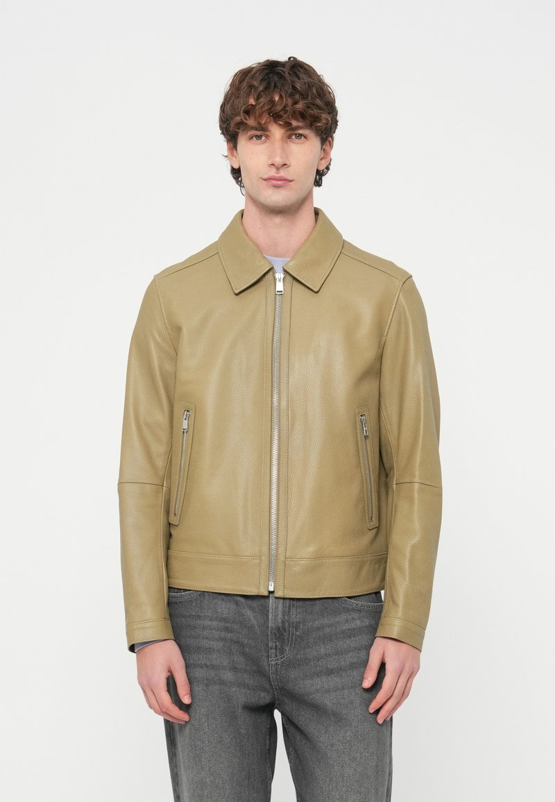 Δερμάτινο μπουφάν ανοιχτό ελιάς με επίπεδη γιακά, κλείσιμο με φερμουάρ και δύο πλαϊνές τσέπες. Ομαλή υφή με εφαρμοστή �σχεδίαση, συνδυασμένο με γκρι τζιν.