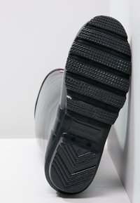 Bota de lluvia de goma negra con suela texturizada y antideslizante. Logo "HUNTER" visible en el talón. Superficie superior lisa con un ligero brillo.
