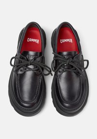 Black leather shoes with round toes and thick black rubber soles. Features black laces and red insoles, branded with "CAMPER."