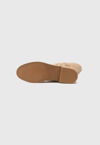 Tan Michael Kors flat shoe shown from bottom, rubber sole with brand name and size 7M, and suede upper with gold chain detail.