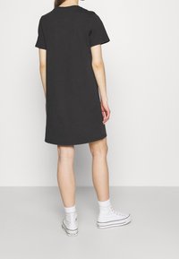 Svart kortärmad t-shirtklänning i bomull, med rund halsringning och avslappnad passform, tillsammans med vita högskor.