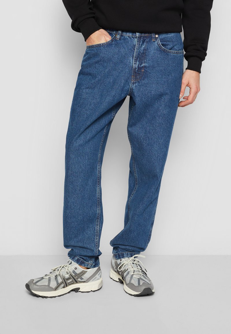 Blå denimjeans med en afslappet pasform, fem-pockets design, kontraststing, og en let falming, parret med grå sportssko.