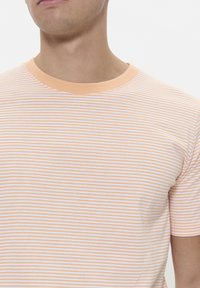 Short-sleeved t-shirt featuring peach and white horizontal stripes, with a round neck and soft cotton texture. Simple and basic design.