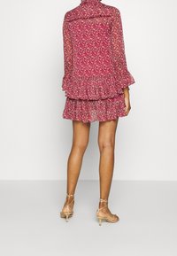 Red floral dress with ruffled hem, sheer fabric, and long sleeves. Paired with nude strappy heels. Back view, displaying design and length.