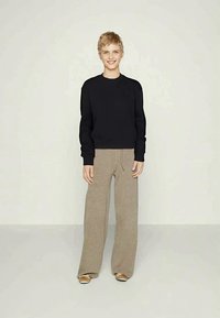 Black crew-neck sweatshirt, beige wide-leg trousers with drawstring waist, soft texture, styled with beige footwear, standing against a neutral background.